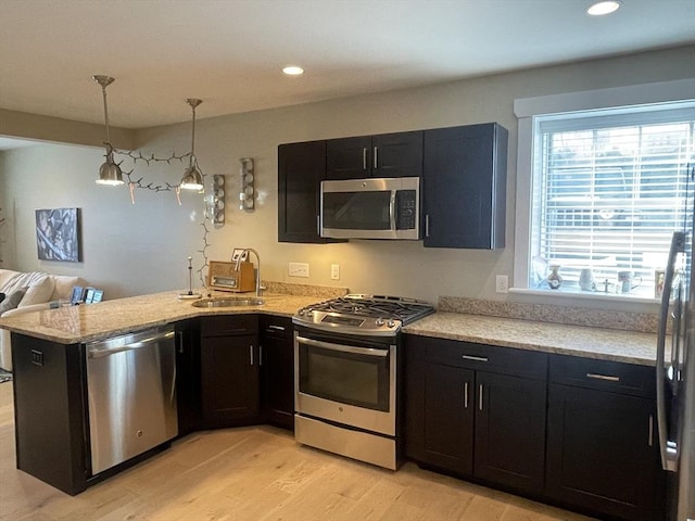 kitchen with kitchen peninsula, stainless steel appliances, sink, pendant lighting, and light hardwood / wood-style floors