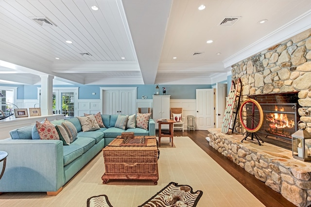 living room with decorative columns, light wood-type flooring, a fireplace, crown molding, and beam ceiling