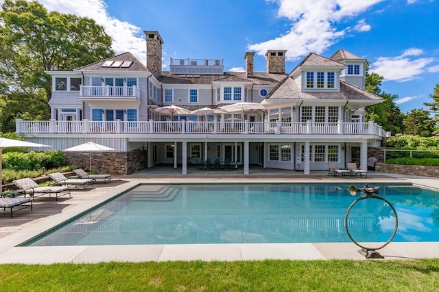 back of property with an outdoor pool, a chimney, french doors, a balcony, and a patio area