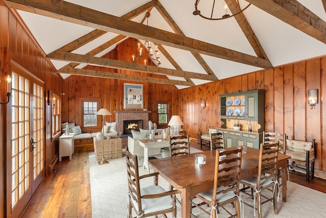 dining room featuring hardwood / wood-style flooring, beam ceiling, wooden walls, and a brick fireplace