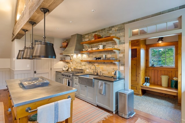 kitchen with range with two ovens, white cabinets, sink, backsplash, and wall chimney range hood