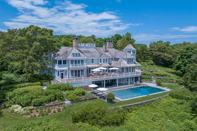 rear view of house featuring an outdoor pool, a balcony, a yard, and a patio