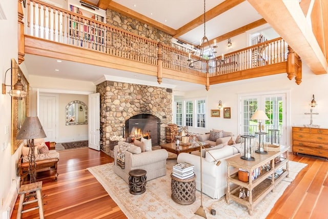living area featuring wood-type flooring, a towering ceiling, beamed ceiling, a notable chandelier, and a fireplace