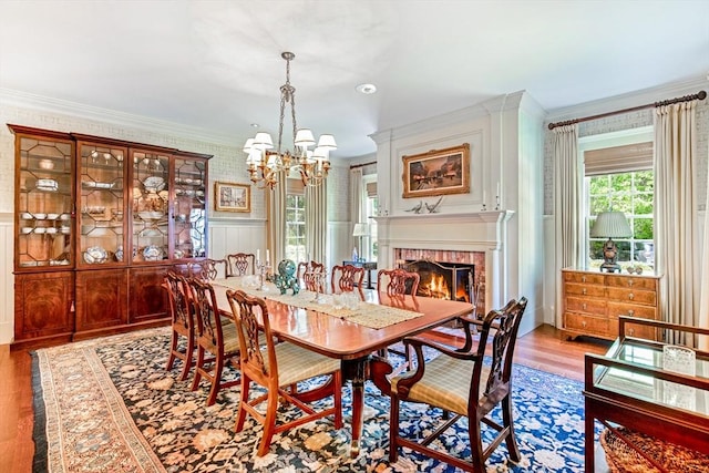 dining room featuring a brick fireplace, crown molding, a chandelier, and wood finished floors