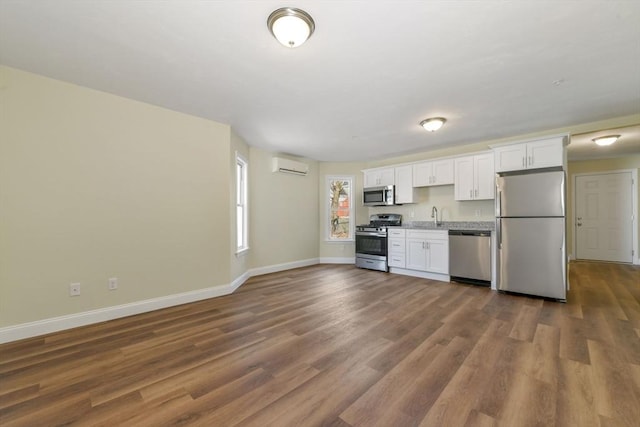 kitchen featuring dark wood-type flooring, white cabinetry, a wall unit AC, appliances with stainless steel finishes, and baseboards