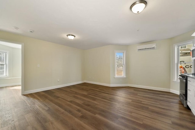 empty room featuring dark wood finished floors, an AC wall unit, and baseboards