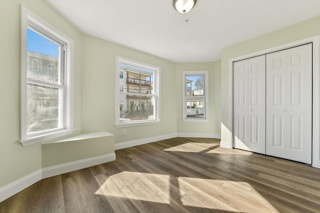 unfurnished bedroom featuring baseboards, multiple windows, and wood finished floors