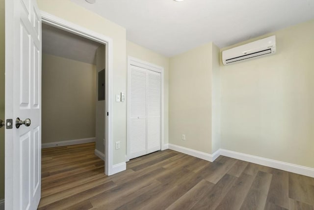 unfurnished bedroom featuring baseboards, a wall mounted air conditioner, electric panel, wood finished floors, and a closet