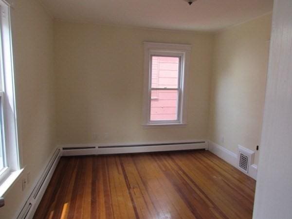 spare room with visible vents, baseboard heating, hardwood / wood-style flooring, and a wealth of natural light