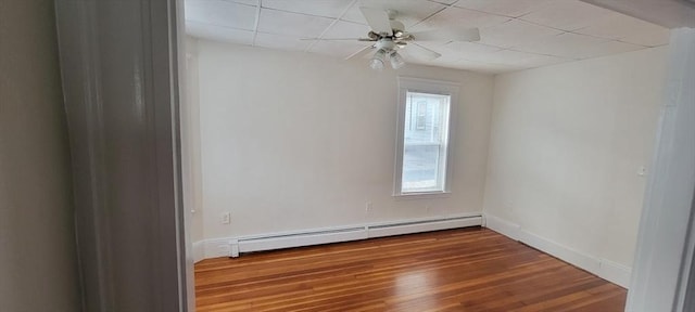 unfurnished room featuring baseboards, baseboard heating, a drop ceiling, and wood finished floors