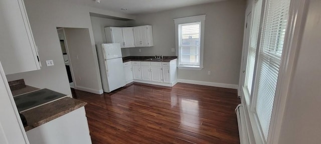kitchen featuring dark wood-type flooring, freestanding refrigerator, a sink, and dark countertops