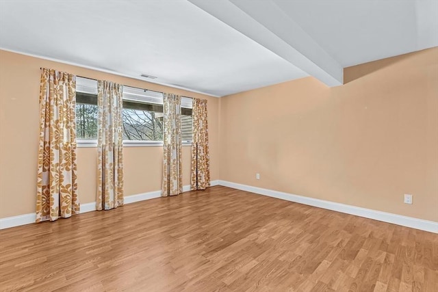 empty room with beam ceiling and light wood-type flooring