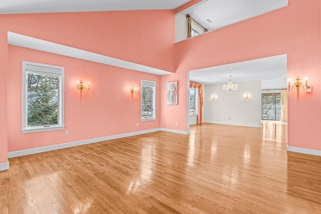 unfurnished living room featuring high vaulted ceiling, light wood-type flooring, and an inviting chandelier