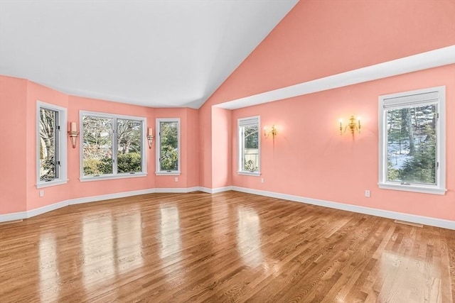 empty room featuring vaulted ceiling, plenty of natural light, and hardwood / wood-style floors