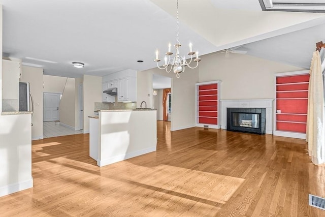 kitchen with backsplash, a tile fireplace, white cabinetry, light wood-type flooring, and a chandelier