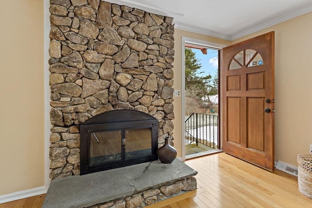 foyer with visible vents, crown molding, a stone fireplace, and wood finished floors