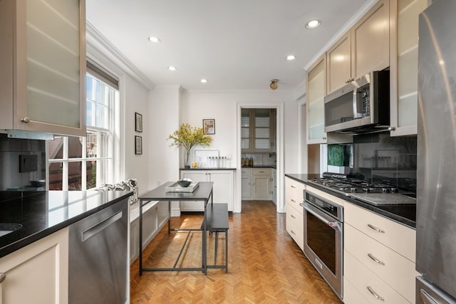 kitchen with light parquet floors, backsplash, appliances with stainless steel finishes, ornamental molding, and dark stone counters