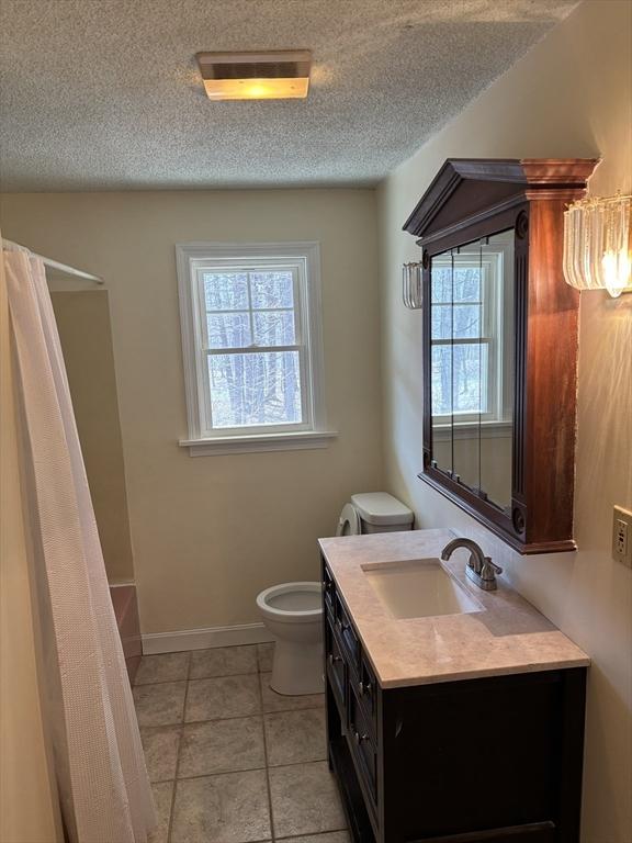 full bathroom with vanity, baseboards, a textured ceiling, curtained shower, and toilet