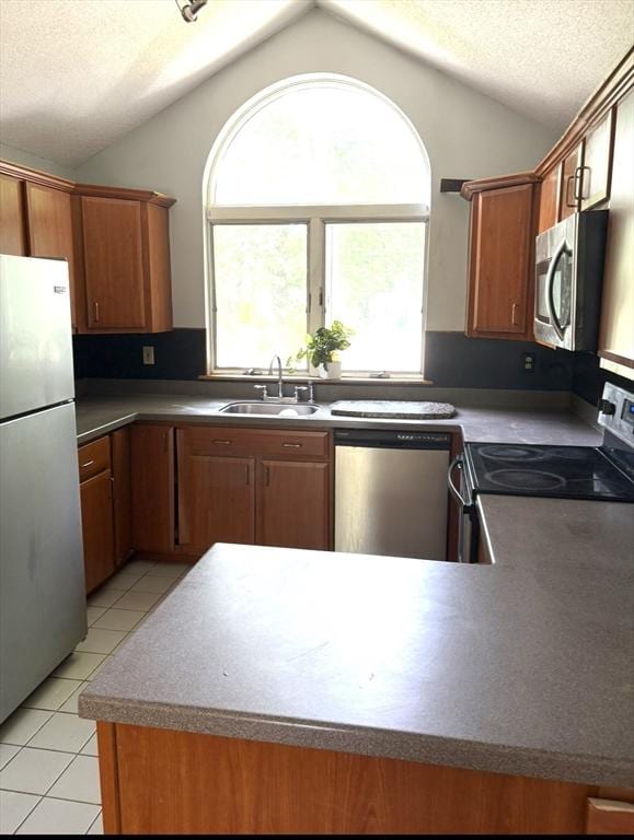 62 Musket, Mashpee, MA 02649 - kitchen with appliances with stainless steel finishes, lofted ceiling, light tile patterned floors, brown cabinetry, and a peninsula