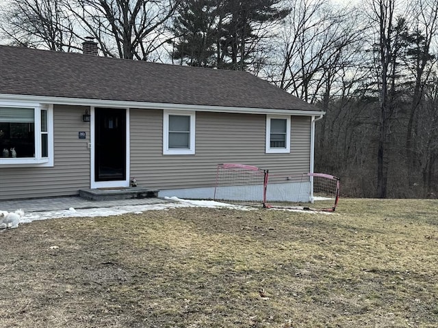 view of front of house with entry steps, roof with shingles, a chimney, and a front lawn