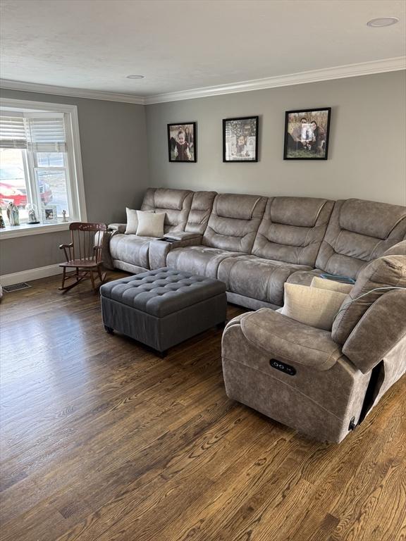 living area featuring baseboards, dark wood finished floors, visible vents, and crown molding