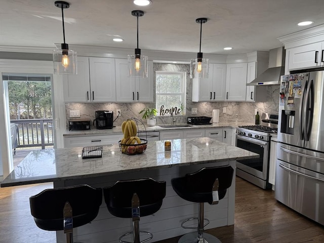 kitchen with a breakfast bar, stainless steel appliances, wall chimney range hood, white cabinetry, and a sink