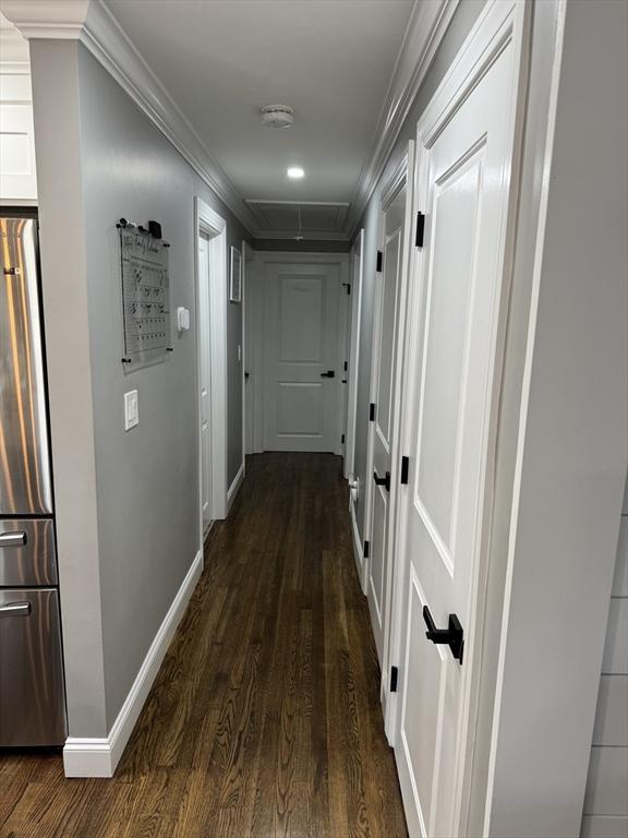 corridor with ornamental molding, dark wood finished floors, attic access, and baseboards