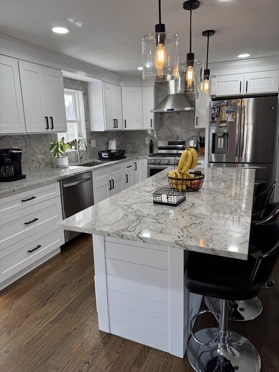 kitchen with stainless steel appliances, a breakfast bar, dark wood-style flooring, white cabinetry, and wall chimney range hood