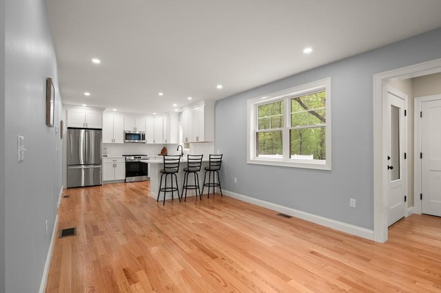kitchen featuring appliances with stainless steel finishes, white cabinetry, a kitchen bar, baseboards, and light wood-style flooring
