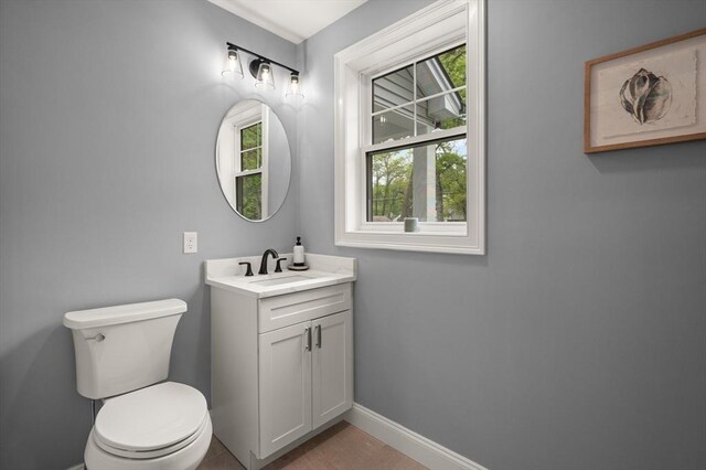 half bathroom with baseboards, toilet, and vanity