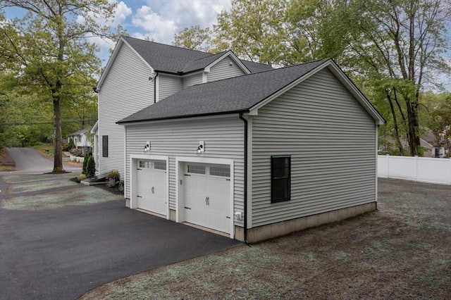 view of side of property featuring roof with shingles, a garage, driveway, and fence