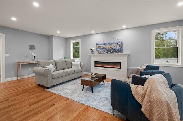 living room with light wood finished floors, a glass covered fireplace, recessed lighting, and baseboards