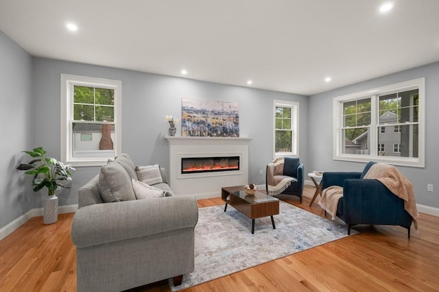 living area with a glass covered fireplace, recessed lighting, wood finished floors, healthy amount of natural light, and baseboards