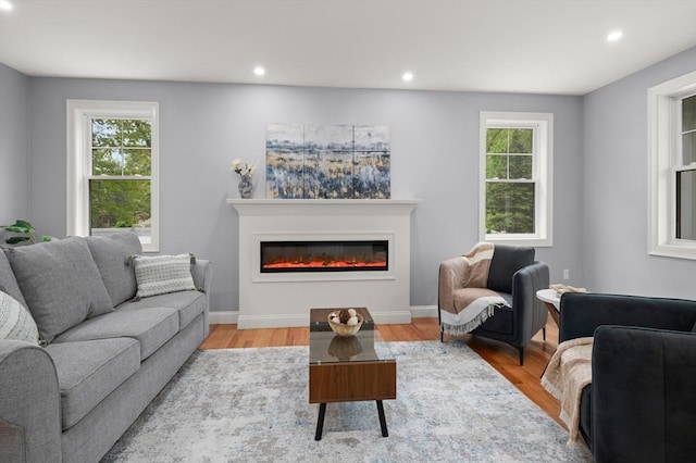 living room featuring a glass covered fireplace, recessed lighting, light wood-style floors, and baseboards