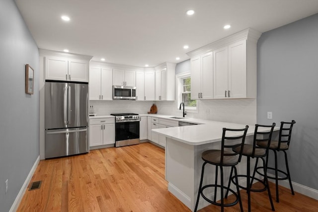kitchen featuring appliances with stainless steel finishes, a sink, a peninsula, light wood-style flooring, and recessed lighting