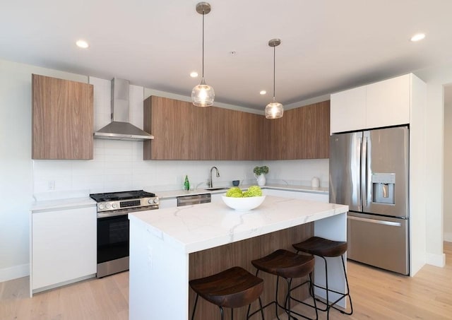 kitchen with wall chimney exhaust hood, stainless steel appliances, decorative light fixtures, light hardwood / wood-style flooring, and a center island