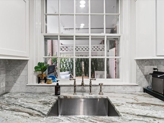 kitchen with light stone counters, white cabinets, a sink, and backsplash