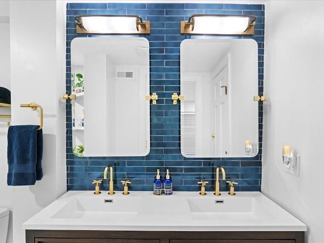 full bath featuring toilet, double vanity, visible vents, and decorative backsplash