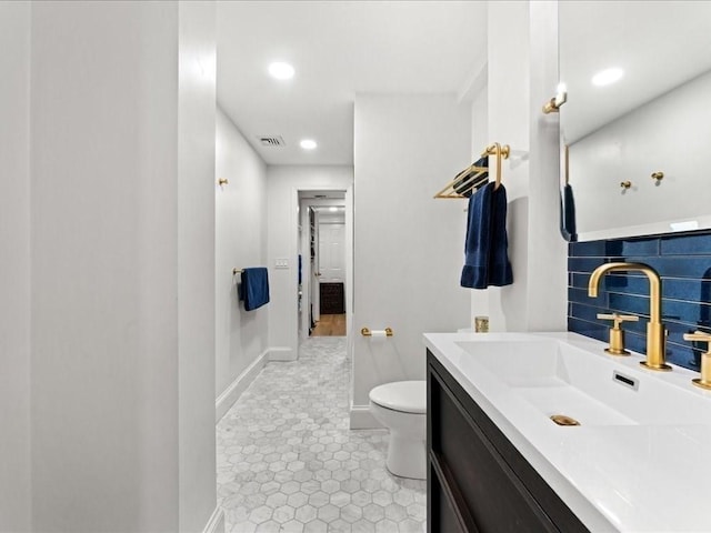 bathroom with toilet, visible vents, vanity, baseboards, and backsplash