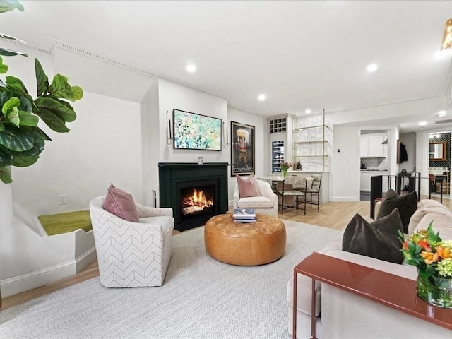 living area with baseboards, a lit fireplace, light wood finished floors, and recessed lighting