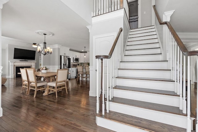 stairway with crown molding, a fireplace, hardwood / wood-style flooring, and a notable chandelier