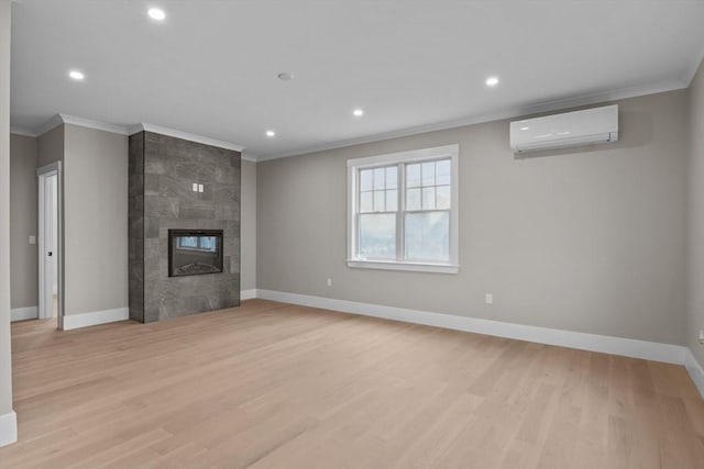 unfurnished living room with light wood-type flooring, an AC wall unit, ornamental molding, and a tile fireplace