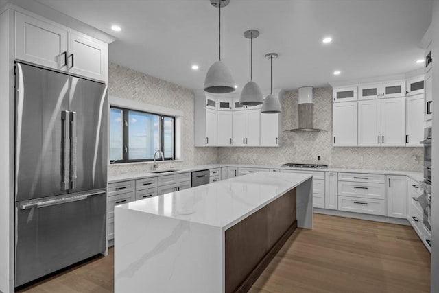 kitchen with a center island, wall chimney exhaust hood, stainless steel appliances, pendant lighting, and white cabinets