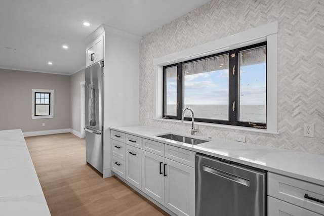 kitchen featuring white cabinetry, sink, stainless steel appliances, light hardwood / wood-style floors, and ornamental molding