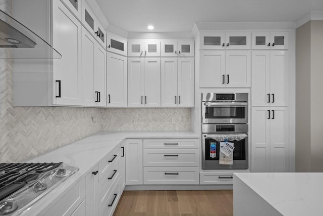 kitchen with backsplash, light hardwood / wood-style flooring, light stone counters, white cabinetry, and stainless steel appliances