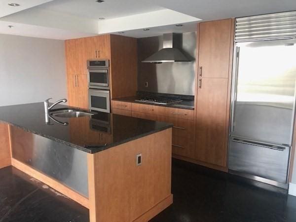 kitchen featuring stainless steel appliances, a sink, wall chimney range hood, brown cabinets, and recessed lighting