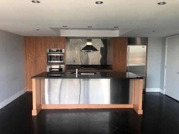 kitchen with brown cabinetry, wall chimney range hood, baseboards, recessed lighting, and appliances with stainless steel finishes