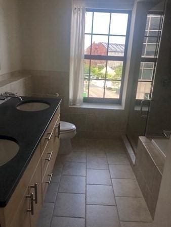 full bath featuring tile patterned floors, double vanity, toilet, tiled bath, and a shower