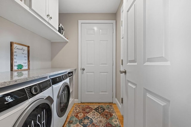 clothes washing area with light wood finished floors, cabinet space, baseboards, and separate washer and dryer