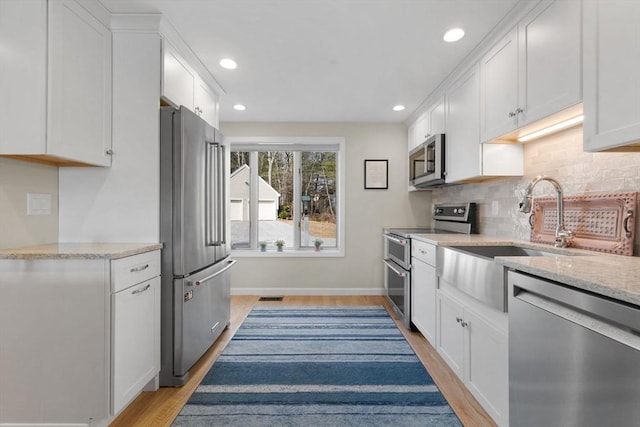 kitchen with light stone counters, light wood-style flooring, stainless steel appliances, white cabinetry, and tasteful backsplash